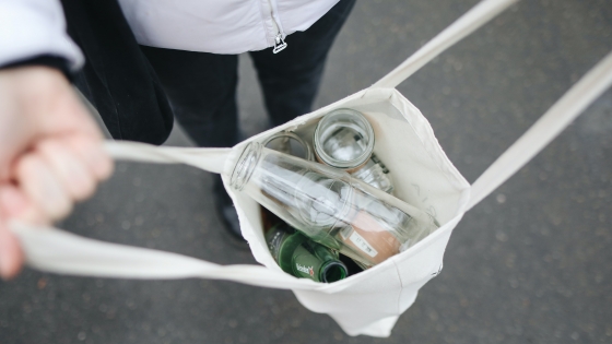 persoon die glazen flessen verzamelt in een herbruikbare tas
